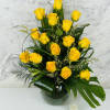 Yellow roses arranged in a glass vase with dark green foliage.