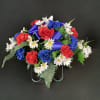 Red, white, and blue floral arrangement with a purple ribbon on a stand