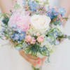 The bouquet features a white rose, paired with a light pink garden