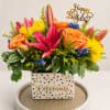 vibrant birthday arrangement featuring bright pink lilies, peach roses, yellow chrysanthemums, blue