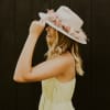 Woman in a light dress wearing a cream hat decorated with pink and white flowers around the crown