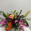 Vivid orange roses and large pink‑purple lilies combine with deep magenta carnations