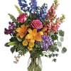 Mixed bouquet with roses, lilies, and blue and pink spikes in a glass vase