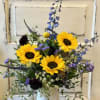 A white washed metal vase holds a summer fresh design featuring sunflowers.