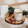 Lit candle in a glass jar on a wood slice with dried petals