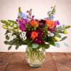 Mixed bouquet of orange, purple, and blue flowers in a clear glass vase