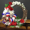 A grapevine wreath dressed in red roses, white daisy-style blooms and delicate