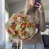 Large bouquet of peach, pink, and cream flowers wrapped in pale paper