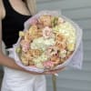 Handheld bouquet of blush roses and pale hydrangeas wrapped in lavender paper