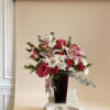 Arrangement of pink lilies, red roses, red carnations, and white daisies in a dark red vase