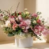 Low arrangement of pink orchids and roses with white and peach blooms in a white ceramic cylinder vase