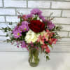 Mixed bouquet of red, pink, purple, and white flowers in a clear glass vase