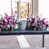 Two pink and lavender floral sprays flank a metal urn on a table