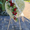 Heart-shaped floral wreath with red roses and white flowers on a stand