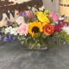 A large sunflower takes center stage in this cheerful low flower arrangement
