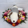 A plush dog nestled in a heart-shaped floral display makes this flower