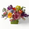 Colorful mixed arrangement of roses, tulips, and other blooms in a green cube vase with a butterfly accent