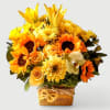 Compact arrangement of yellow and orange sunflowers, roses, lilies and other blooms in a burlap-wrapped cube vase