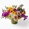 Bright mixed arrangement of roses, gerbera daisies, orchids, and other blooms in a green cylinder vase