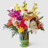 Tall mixed bouquet of bright roses, lilies, orchids, and other blooms in a glass vase with green ribbon.