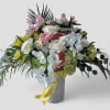 Tall arrangement of white orchids, roses, and mixed blooms in a textured vase with yellow ribbon.