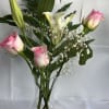 Soft pink rosebuds mingle with bright white lilies in a clear glass