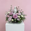 A front-facing arrangement featuring lavender, pink, and white blooms with a keepsake