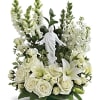 White roses and lilies arranged around a small statue in a vase