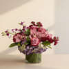 Low arrangement of pink roses and orchids with purple hydrangea in a leaf-lined glass vase