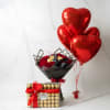 Red heart balloons beside a bouquet of red roses and a Ferrero Rocher gift box