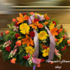 Large round spray of orange lilies, yellow gerberas, roses, and red carnations with a lavender bow.