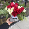 Red and white roses arranged with evergreen branches in a small holiday container.
