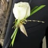 White rose boutonniere with green accents on a dark suit lapel