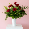 Red roses arranged in a white vase with green foliage