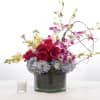Low arrangement of red roses, purple orchids, and blue hydrangeas in a glass vase with a small white candle.