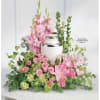 A soft pastel tribute arranged around a white cremation urn, this sympathy
