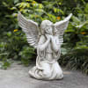 White angel statue kneeling with folded hands in a garden setting