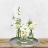 Three small white floral arrangements in clear glass vases on a metal tray