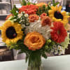 Bouquet of sunflowers, orange roses, and white hydrangeas in a glass vase