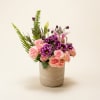 Soft pink roses mingle with vivid purple daisy-like blooms and pale lilies