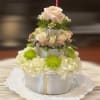 Tiered floral cake with cream roses and white hydrangeas on a doily-lined plate