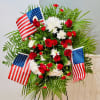 A formal standing spray composed of deep red roses, red carnations, and