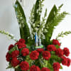 Red carnations with white flowers and a small Lourdes statue in a wooden container