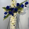Cross-shaped floral tribute with white chrysanthemums and blue roses on an easel