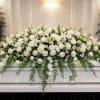 A serene, all-white casket spray designed to honor a loved one with