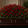 A dense sweep of deep red roses laid across a casket creates