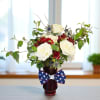 Patriotic red, white, and blue flower arrangement in a red vase with a star-spangled bow.
