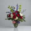 Red roses and white daisies in a glass vase with a patriotic ribbon