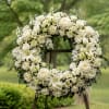A large, all-white funeral wreath crafted to convey calm and reverence, this