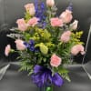 Tall mixed bouquet of pink roses and carnations with blue delphinium in a green vase with purple bow
